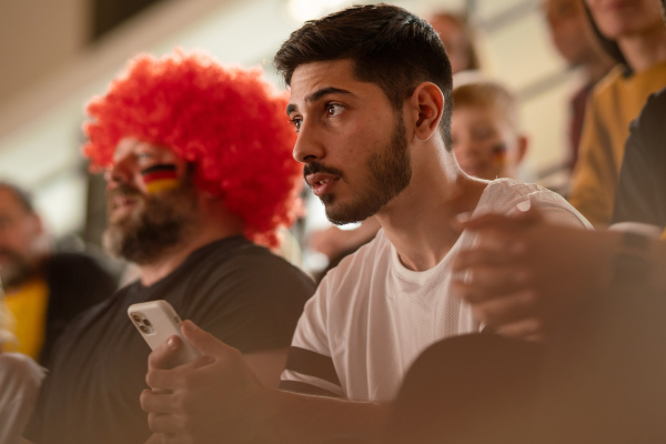 Worried football fans supproting a German national team in live soccer match at stadium.