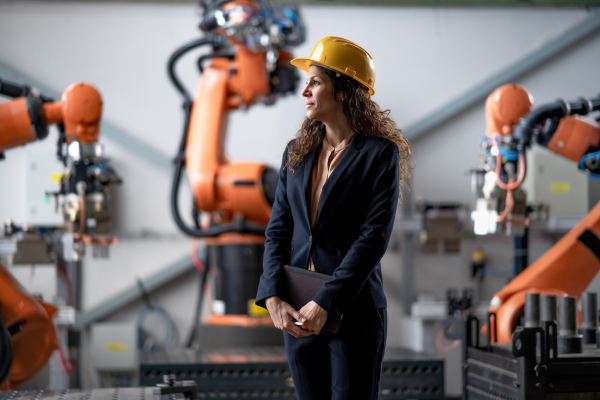 An automation female engineer with tablet for programming robotic arm in factory.