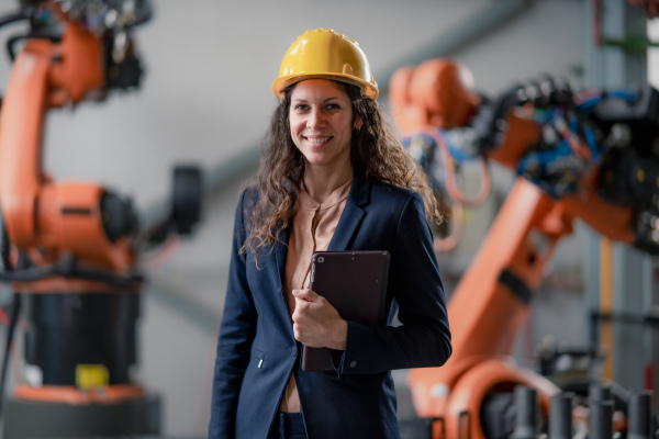 An automation female engineer with tablet for programming robotic arm in factory.