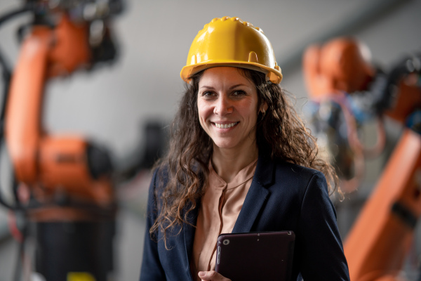 An automation female engineer with tablet for programming robotic arm in factory.