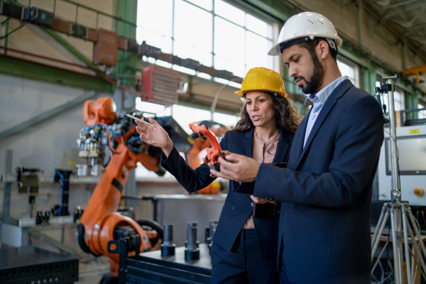 A man engineer holding model of industrial robotic arm and showing to collegue in factory.