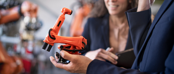 A close-up of man engineer holding model of industrial robotic arm and showing to collegue in factory.