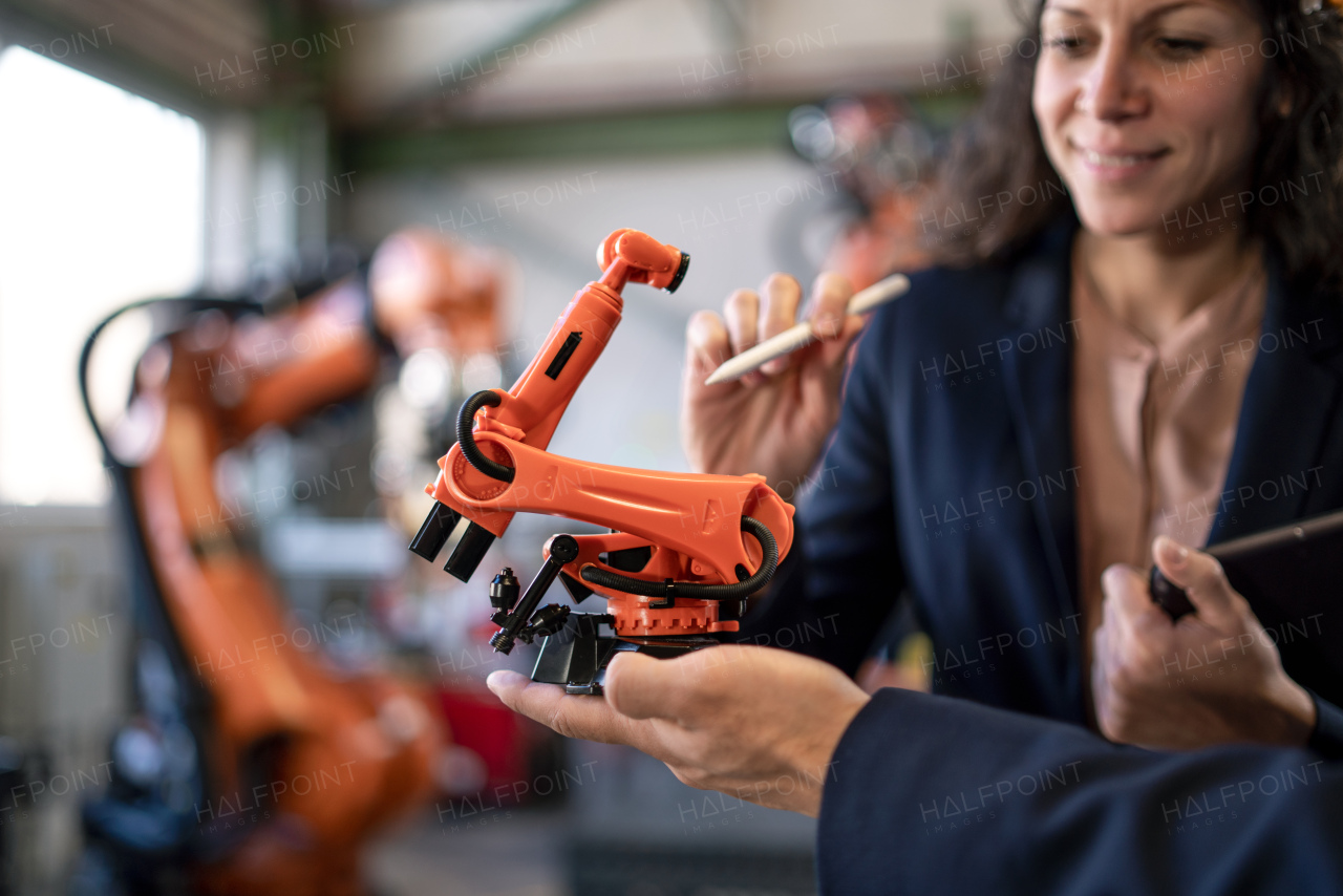 A close-up of man engineer holding model of industrial robotic arm and showing to collegue in factory.