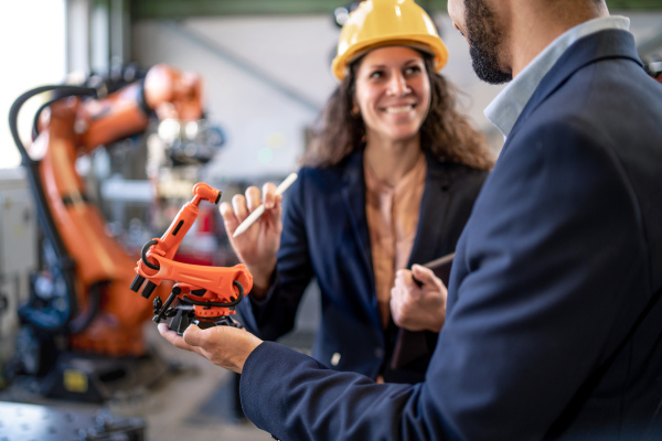 A man engineer holding model of industrial robotic arm and showing to collegue in factory.