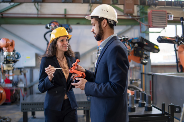 A man engineer holding model of industrial robotic arm and showing to collegue in factory.