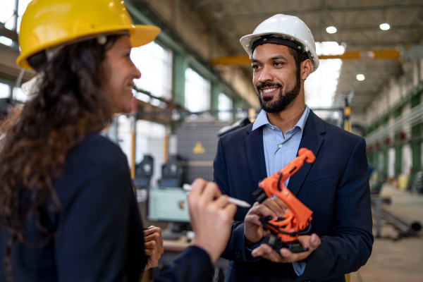 A man engineer holding model of industrial robotic arm and showing to collegue in factory.