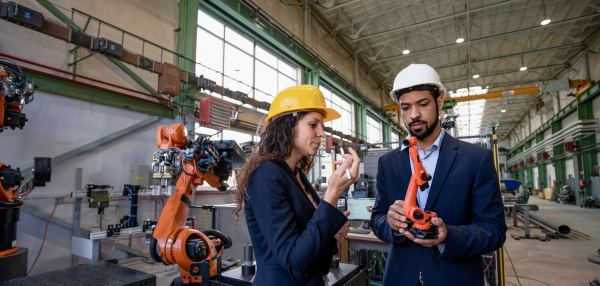 A man engineer holding model of industrial robotic arm and showing to collegue in factory.