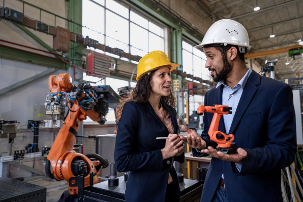 A man engineer holding model of industrial robotic arm and showing to collegue in factory.