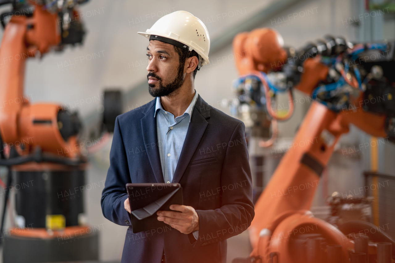 An automation engineer uses tablet for programming robotic arm in factory.