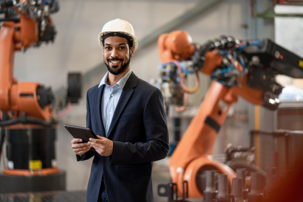 An automation engineer uses tablet for programming robotic arm in factory.