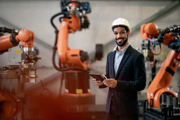 An automation engineer uses tablet for programming robotic arm in factory.