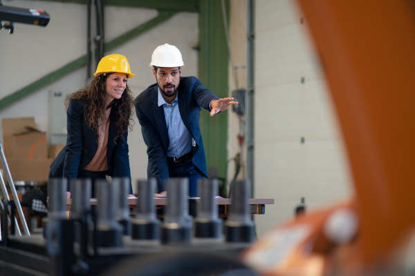 A chief engineer and project manager in modern industrial factory with robot arms talking and planning optimization of production.