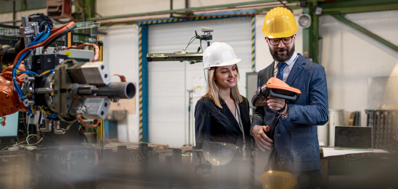 A chief engineer and project manager in modern industrial factory with robot arms talking and planning optimization of production.