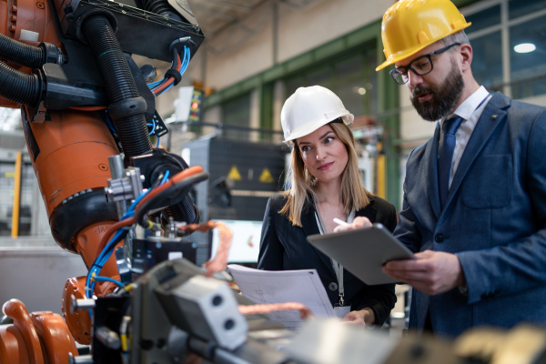 A chief engineer and project manager in modern industrial factory with robot arms talking and planning optimization of production.