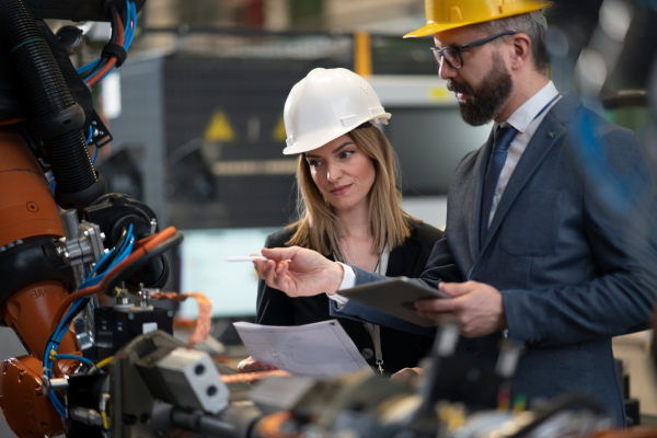 A chief engineer and project manager in modern industrial factory with robot arms talking and planning optimization of production.