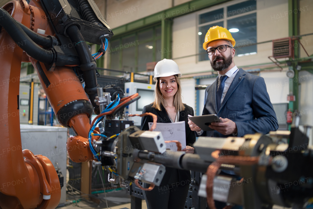 A chief engineer and project manager in modern industrial factory with robot arms talking and planning optimization of production.