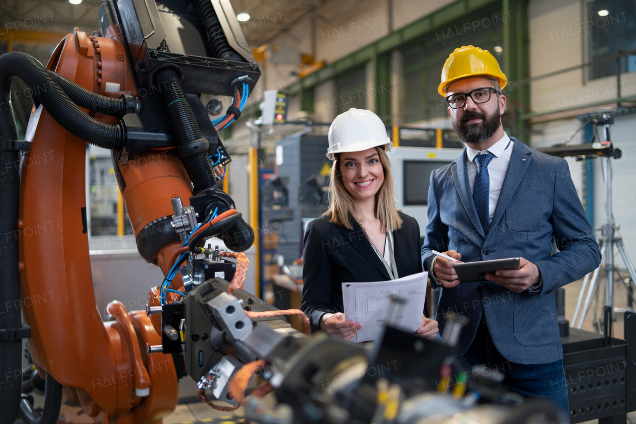 A chief engineer and project manager in modern industrial factory with robot arms talking and planning optimization of production.