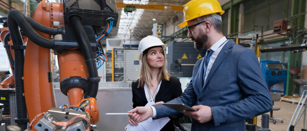 A chief engineer and project manager in modern industrial factory with robot arms talking and planning optimization of production.