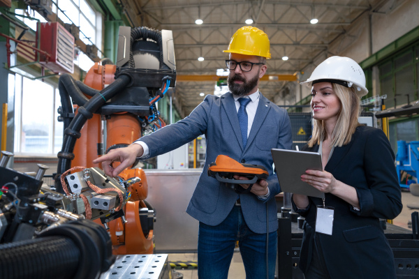 A chief engineer and project manager in modern industrial factory with robot arms talking and planning optimization of production.