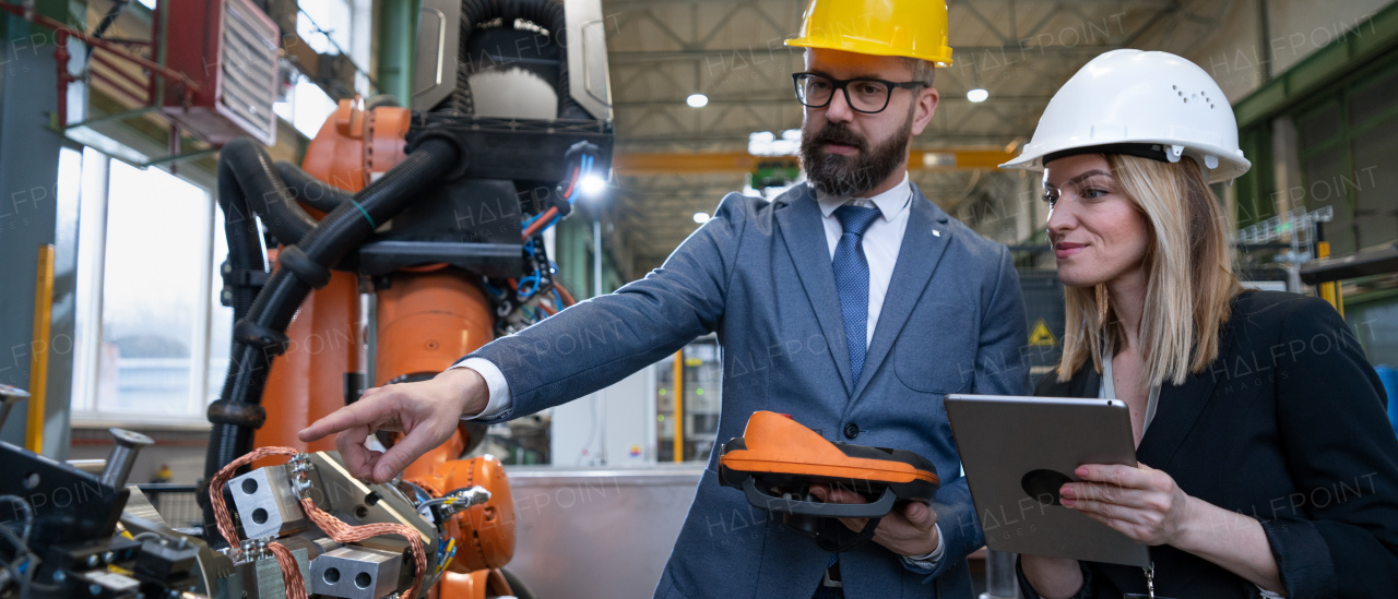 A chief engineer and project manager in modern industrial factory with robot arms talking and planning optimization of production.