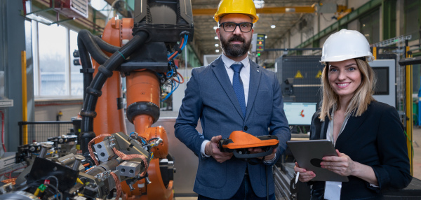 A chief engineer and project manager in modern industrial factory with robot arms talking and planning optimization of production.