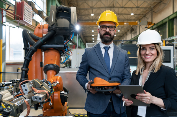 A chief engineer and project manager in modern industrial factory with robot arms talking and planning optimization of production.