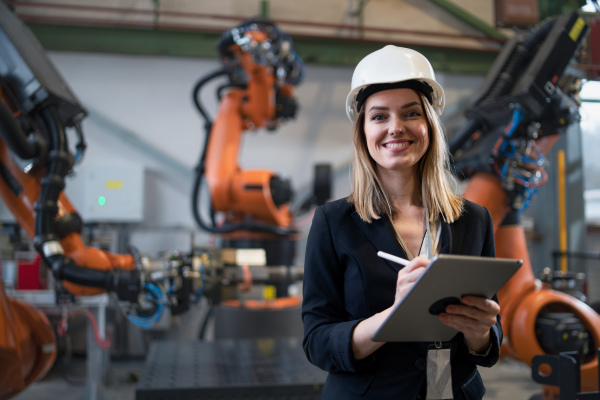 A female chief engineer in modern industrial factory using tablet and making audit. Long angle view.