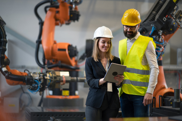 A chief engineer and project manager in modern industrial factory with robot arms talking and planning optimization of production.