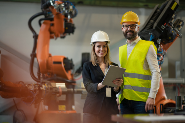 A chief engineer and project manager in modern industrial factory with robot arms talking and planning optimization of production.