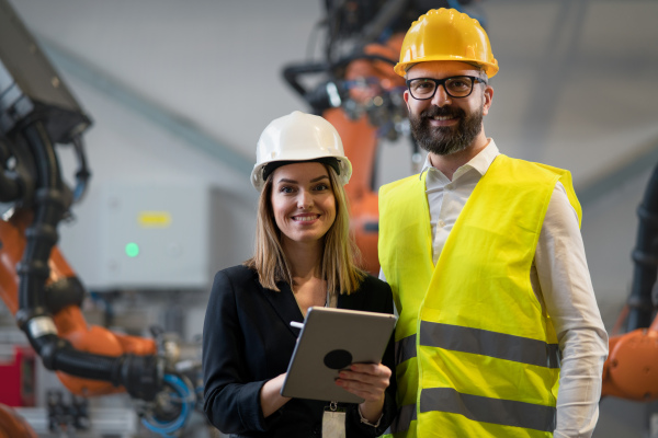 A chief engineer and project manager in modern industrial factory with robot arms talking and planning optimization of production.