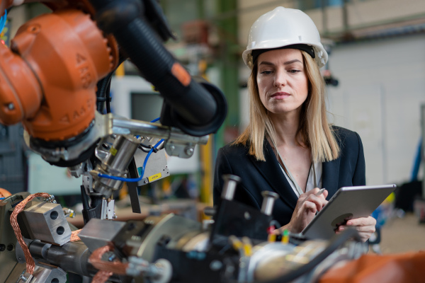 A female chief engineer in modern industrial factory using tablet and making audit. Long angle view.