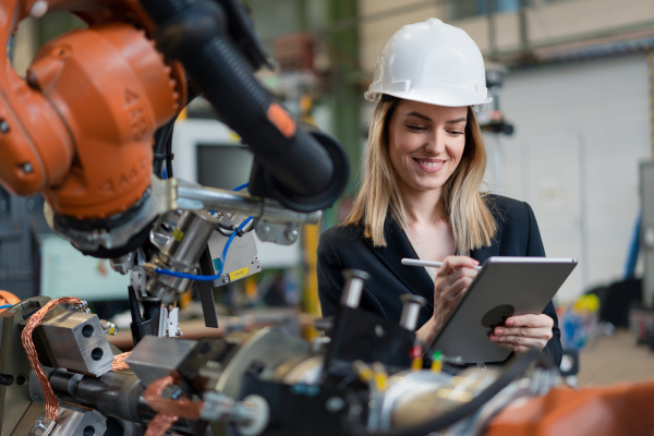 A female chief engineer in modern industrial factory using tablet and making audit. Long angle view.