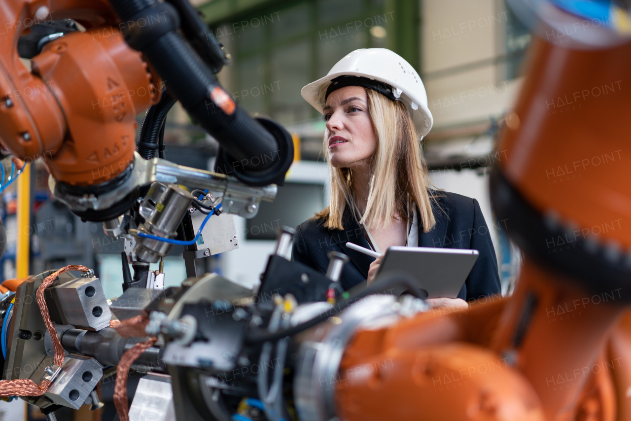 A female chief engineer in modern industrial factory using tablet and making audit. Long angle view.