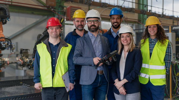 A young man worker with Down syndrome with manager and other collegues working in industrial factory, social integration concept.