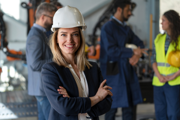 A portrait of female chief engineer in modern industrial factory looking at camera.