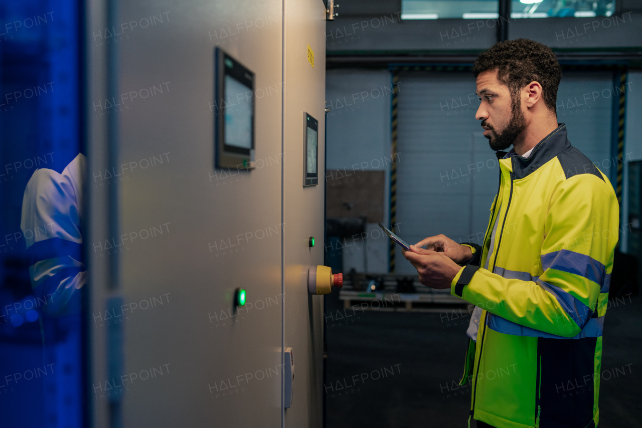 A young industrial worker operating cnc machine at metal machining industry