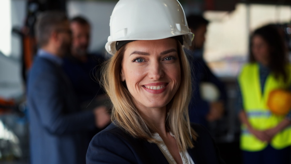 A portrait of female chief engineer in modern industrial factory looking at camera.