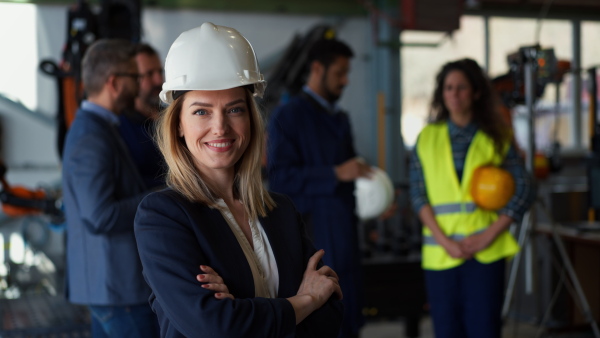 A portrait of female chief engineer in modern industrial factory looking at camera.