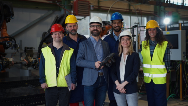 A young man worker with Down syndrome with manager and other collegues working in industrial factory, social integration concept.