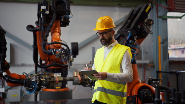 An automation engineer holding scanner in industrial factory and doing control with tablet,