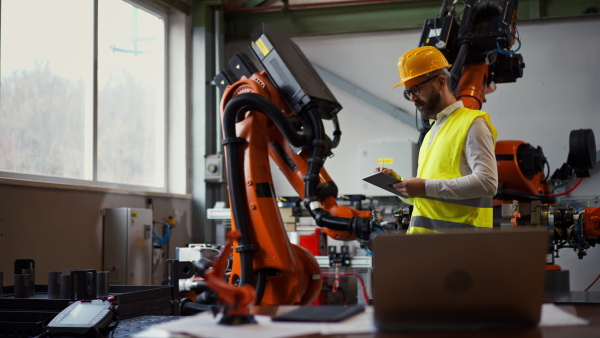 An automation engineer holding scanner in industrial factory and doing control with tablet,