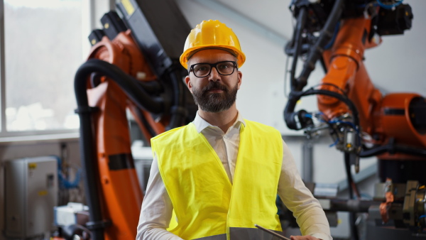 An automation engineer holding scanner in industrial factory and doing control with tablet, looking at camera