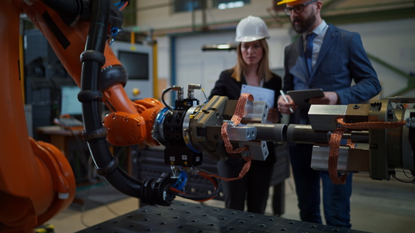 A chief engineer and project manager in modern industrial factory with robot arms talking and planning optimization of production.