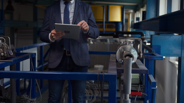 A cut out of chief Engineer using tablet for control and standing in inustrial factory.