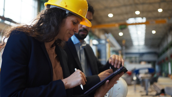 A chief engineer and project manager in modern industrial factory with robot arms talking and planning optimization of production.