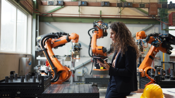 An automation female engineer with tablet for programming robotic arm in factory.