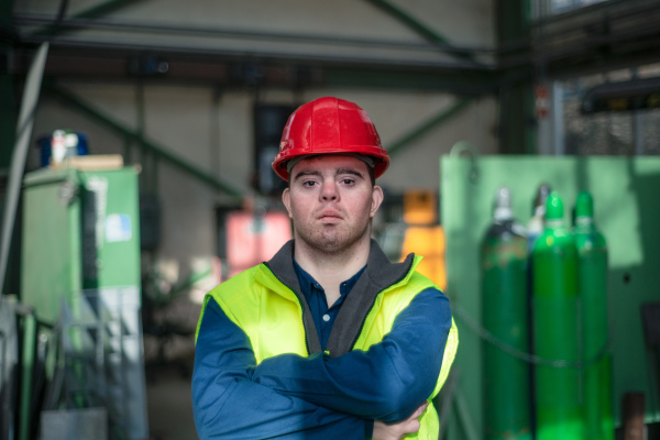 A young man with Down syndrome working in industrial factory, social integration concept.