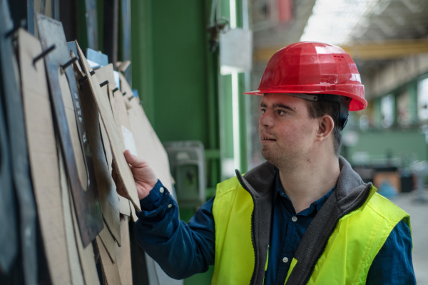 A young man with Down syndrome working in industrial factory, social integration concept.