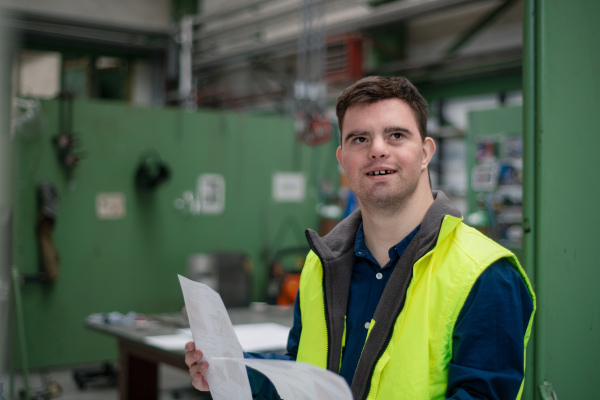 A young man with Down syndrome looking at blueprints when working in industrial factory, social integration concept.