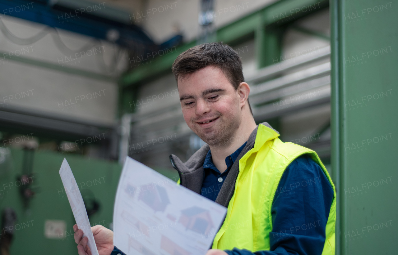 A young man with Down syndrome looking at blueprints when working in industrial factory, social integration concept.